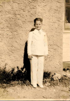 A young boy in uniform standing next to a wall.