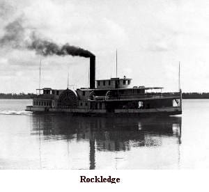 A steam boat on the water with smoke coming out of it.